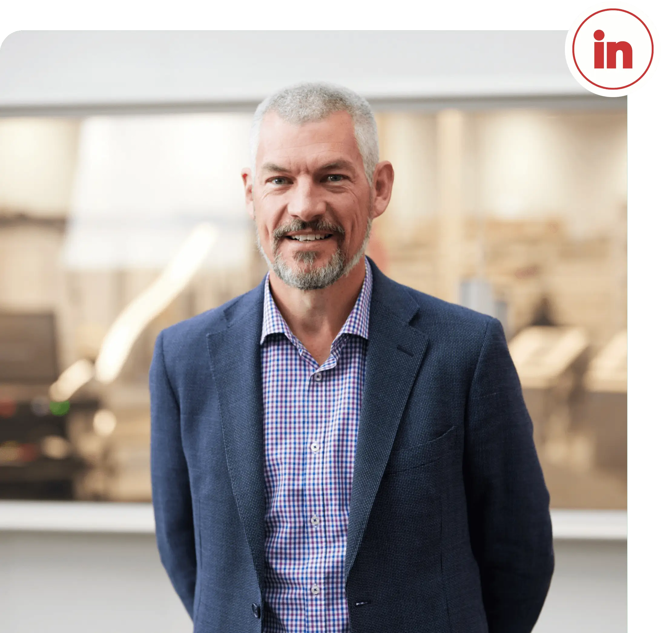 Waist-up photo of Justin Kahl, Executive General Manager of SAGE Automation. He is smiling, looking directly at the camera, and sporting a crisp purple checked shirt and charcoal blazer.