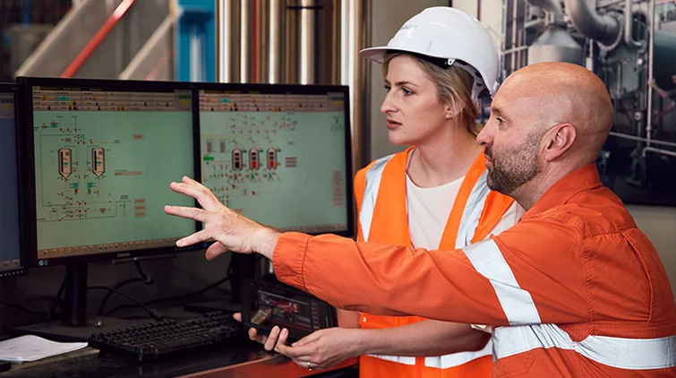 Two engineers monitoring digital screens on a manufacturing site.